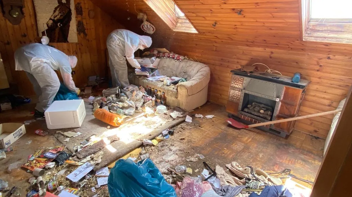 Dachzimmer voller Unrat, zwei Mitarbeiter in Schutzanzügen räumen