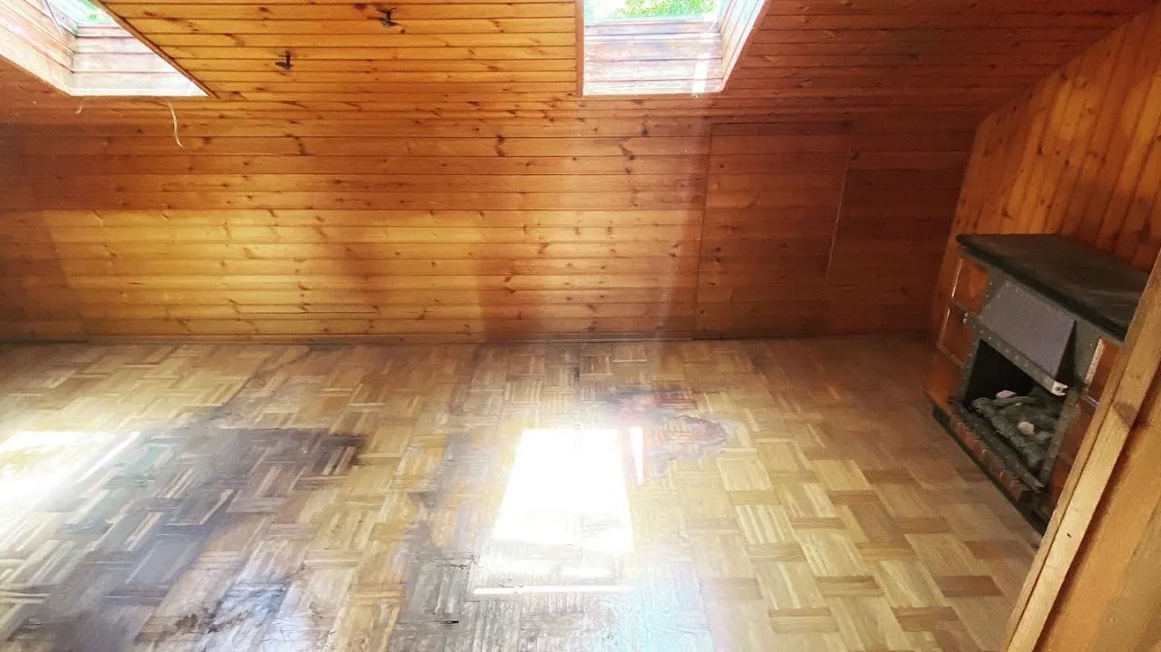 Dasselbe Dachzimmer nach der Entrümpelung, leerer Parkettboden und der Kachelofen