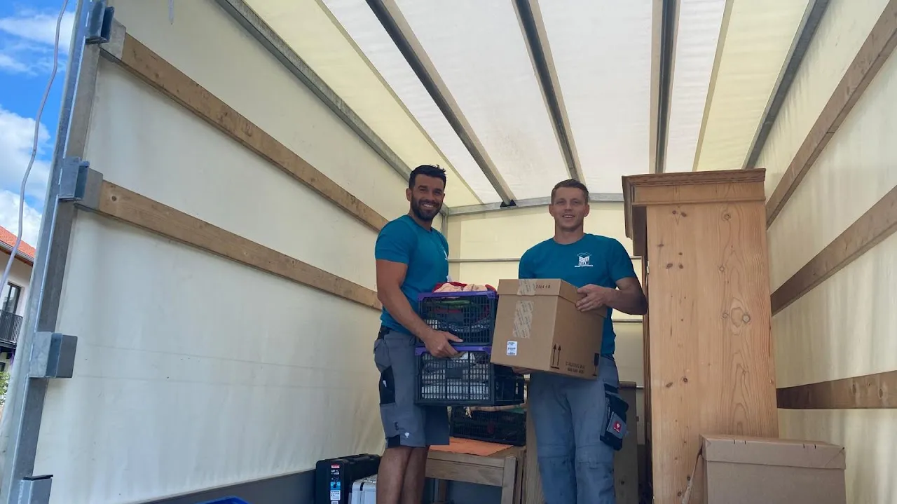 Zwei Mitarbeiter von SM Team laden Kisten und einen Schrank in den Möbelwagen